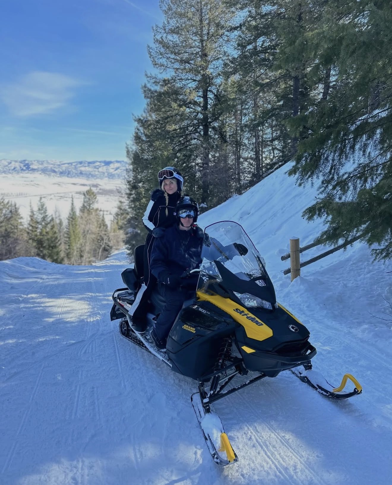 Two people riding yellow snowmobile on snowy trail